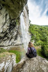 Hiker woman sitting on a rock with backpack while admiring the s