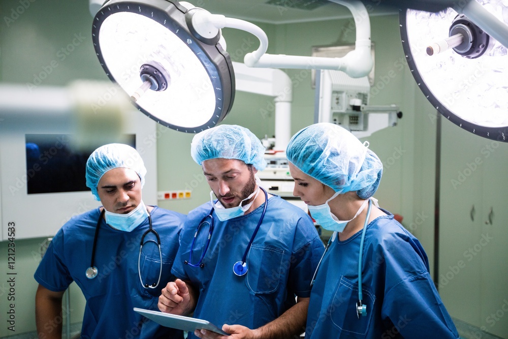 Poster surgeons discussing over digital tablet in operation room