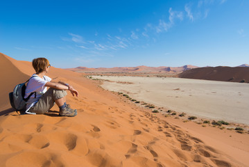 Relaxed tourist sitting on sand dunes and looking at the stunning view in Sossusvlei, Namib desert, best travel destination in Namibia, Africa. 