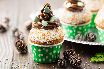 Christmas vanilla Cupcakes with chocolate buttercream icing and holiday decorations on the rustic wooden table, selective focus