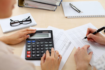 Two female accountants counting on calculator income for tax form completion hands closeup. Internal Revenue Service inspector checking financial document. Planning budget, audit  concept