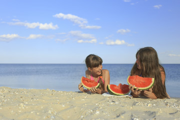 Happy children on the beach eating sweet watermelon.