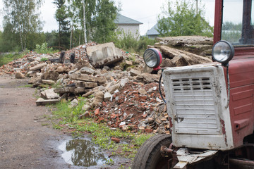 Old red tractor stands near a pile of construction debris