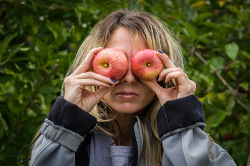 Young woman being silly holding apples to her eyes during family trip to pick apples at an apple farm