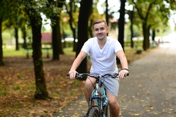 Naklejka premium Blonde attractive young man cycling in the park 