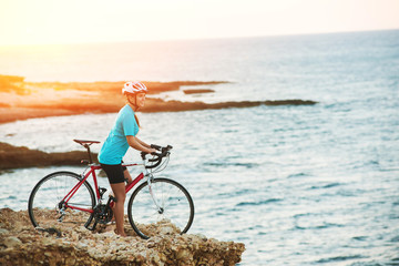 Female cyclist standing on a rock and looking at sea