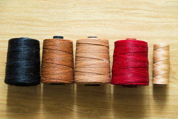 Many colored sewing threads of leather crafting on wood table.