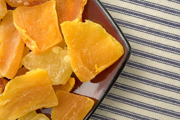 Plate of sugared pineapple, mango and papaya atop a striped tablecloth at an angle.