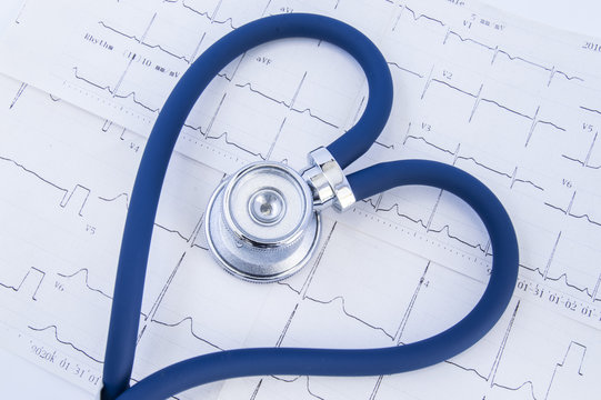Heart formed stethoscope against background of electrocardiogram (ekg). Head or chestpiece and flexible tubing of blue stethoscope folded into heart shape, which lies on printed electrocardiogram 