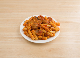 Rigatoni pasta with meatballs and sausage on a plate atop a wood table.