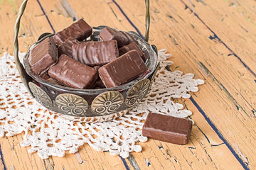 Chocolate candies.   Vase with chocolate candies on openwork napkin on old wooden table.