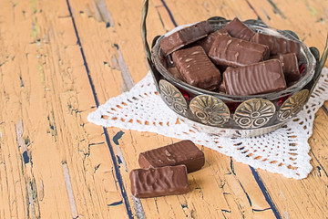 Chocolate candies.   Vase with chocolate candies on openwork napkin on old wooden table.