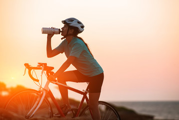 Silhouette of female cyclist riding bike and dringking water with sea on background