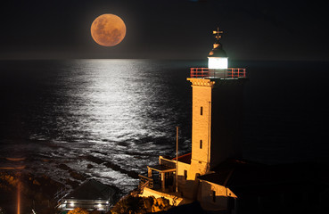 A full moon rising over the sea with a lighthouse in the foreground  © Fiona