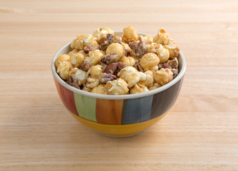 Gourmet popcorn with nuts in a colorful bowl on a wood table.