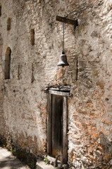 Old wooden door with a small bell above it,in stone  wall. Greece