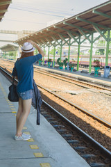 beautiful woman carrying her bag and hat waiting for a train at a railway stationvacation concept