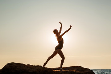 Beautiful ballerina dancing, posing on rock at beach, sea background.