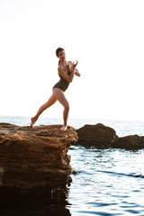 Fototapeta na wymiar Beautiful ballerina dancing, posing on rock at beach, sea background.