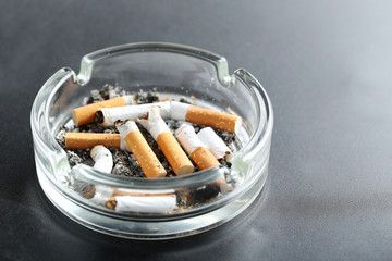 Cigarette butts with ash in ashtray on black background