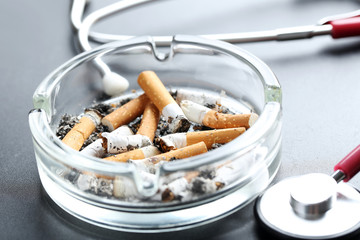 Cigarette butts with ash in ashtray on black background