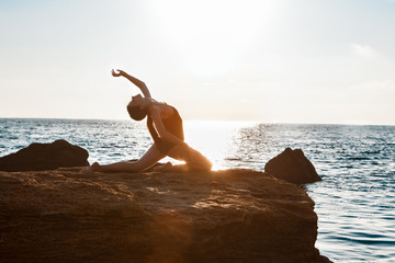 Beautiful ballerina dancing, posing on rock at beach, sea background.