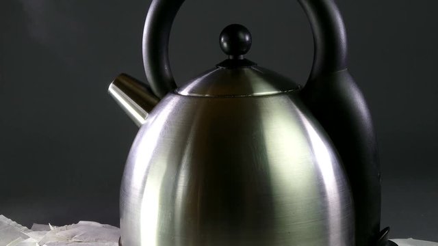 Upward slide of teabags and steam from a stainless steel boiling kettle. 