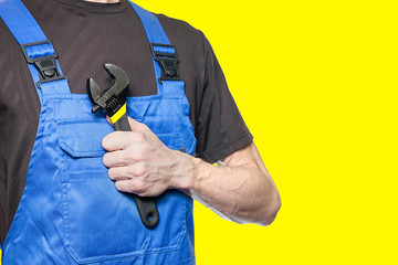 Man mechanic in working clothes holds a wrench in his hand isolated on yellow background