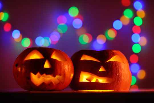 Two Halloween pumpkins head jack lantern with colorful lights on background