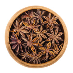 Star anise seeds in a wooden bowl over white. Dried fruits of Illicium verum, also Chinese star anise or badiam. Closely resembles anise in flavor. Used for baking, sambuca, pastis and absinthe.