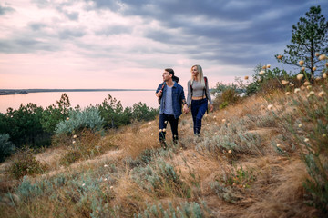 Young caucasian couple hiking outdoors with backpacks during sunset