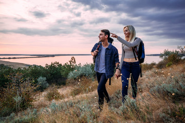 Young caucasian couple hiking outdoors with backpacks during sunset