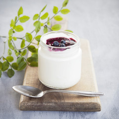 Jar with yogurt, bilberry jam and fresh blueberries. Composition on wooden desk with tea spoon. Selective focus. Shallow depth of field.