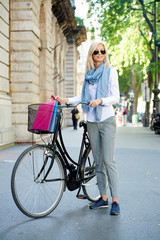 Going to work with bike. Full length portrait of a beautiful blond businesswoman with a cycle walking down the city.