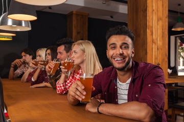 Young People Group In Bar, Drink Beer, Hispanic Man Hold Glass Toasting, Friends Sitting At Wooden Counter Pub