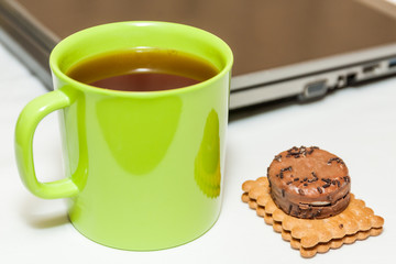 Biscuits and tea in green cup with laptop as background