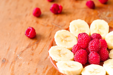Sliced banana with raspberries on the brown plate. horizontal, top view.