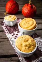 Pumpkin mug-cakes in rustic style, on an old wooden table, next to a pumpkin