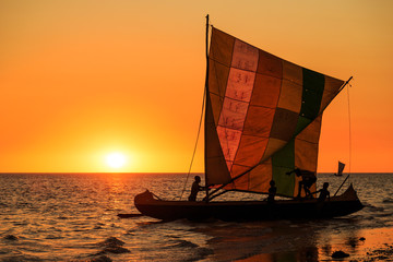 Fishermen in a sailboat on the beach at a beautiful warm orange