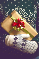 Girl holds in hands Christmas present. Christmas background. Gifts for men. Knitted mittens. Knitted dress. Box with gifts. Merry Christmas. Toned image.