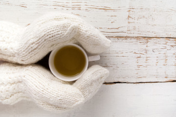 Woman's hands in gloves holding a cup of tea white wooden table