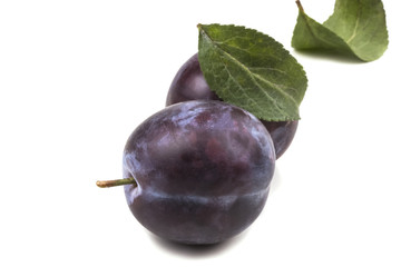 Two ripe appetizing blue fallen plum with green leaves