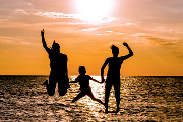 Silhouettes of mother and kids jumping on beach at sunset