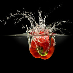 Red bell pepper falling in water with splash on black background