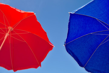 Red and blue beach umbrella and blue sky above. Summer beach vacations