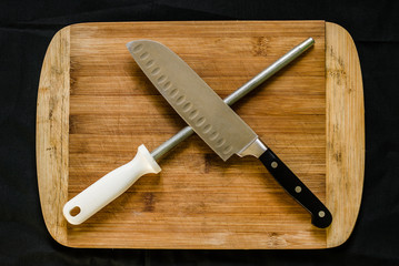 Flay lay photo of a knife sharpener (honing steel) and a chef’s knife on a cutting board against...