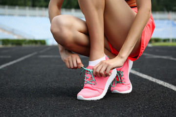Woman tying lace on her sneakers on a running stadium