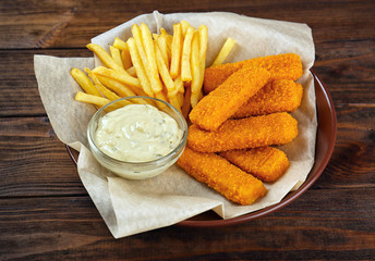 Plate with tasty fish nuggets, fries and sauce on wooden table