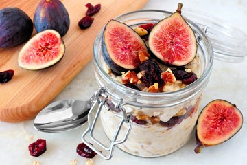 Jar of overnight autumn oats with red figs, cranberries and walnuts against a marble background