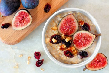 Autumn oatmeal with red figs, cranberries and walnuts in a bowl, overhead scene on white marble